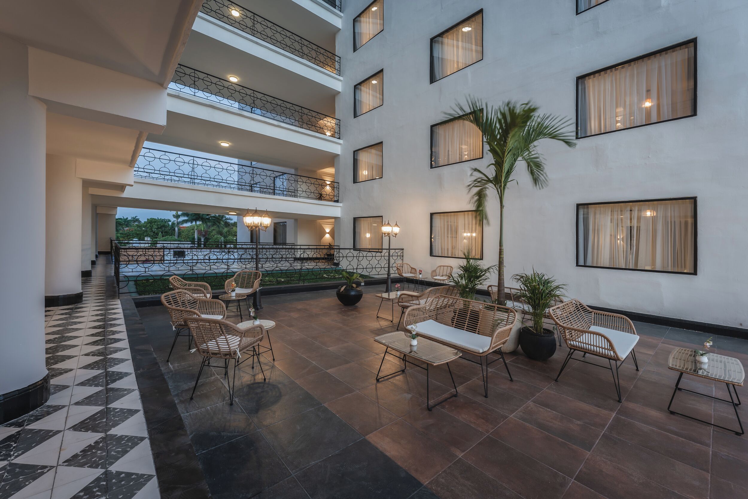 A multi-level hotel lobby with a checkered floor pattern, multiple seating areas with wicker furniture, and a view of the outdoors through large windows.