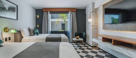 Habitación de hotel con dos camas, un televisor grande, una zona de comedor y piso a cuadros.