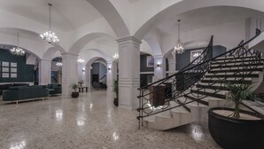 Eine geräumige Lobby mit Marmorboden, einer imposanten Treppe mit Metallgeländer und edlen Kronleuchtern.