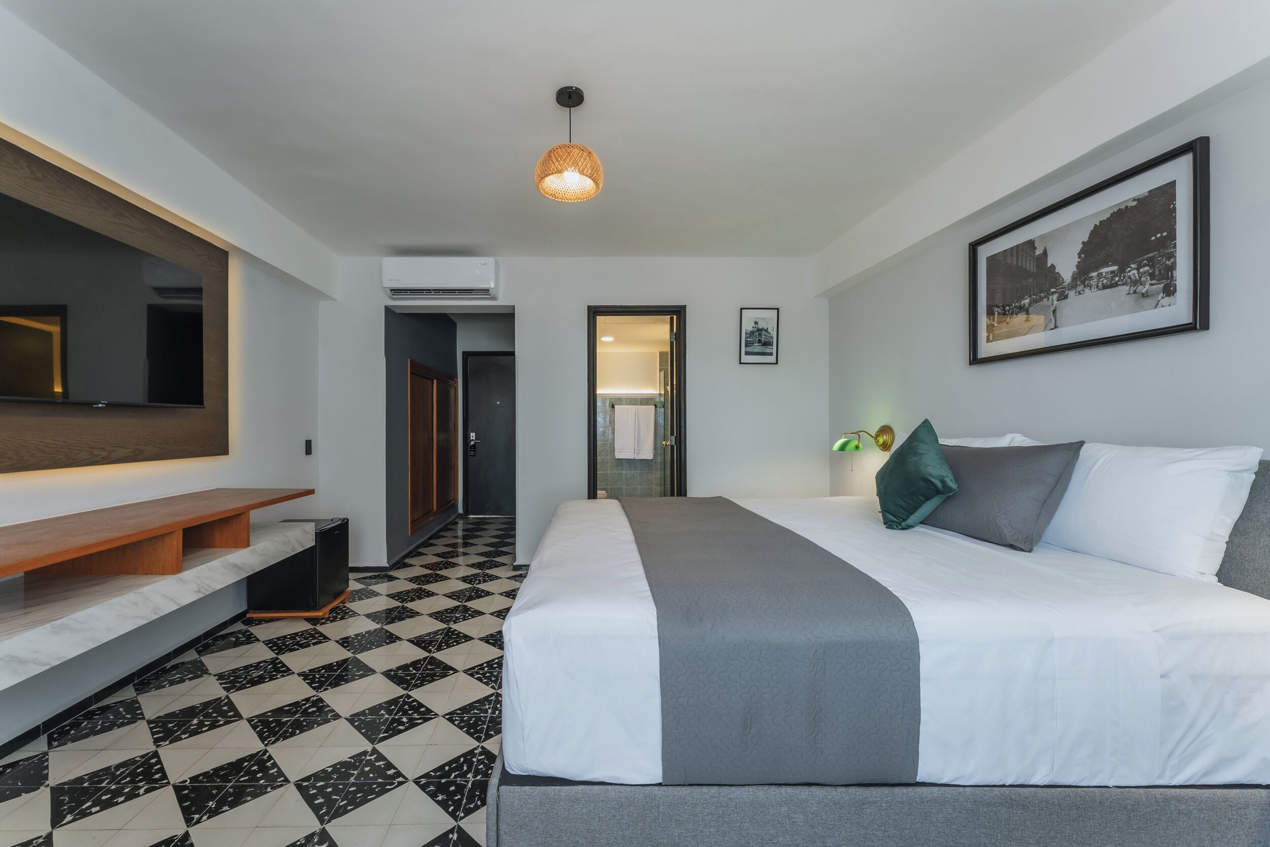A modern hotel room with a large bed, a bench, a flat-screen TV, and a checkered floor.