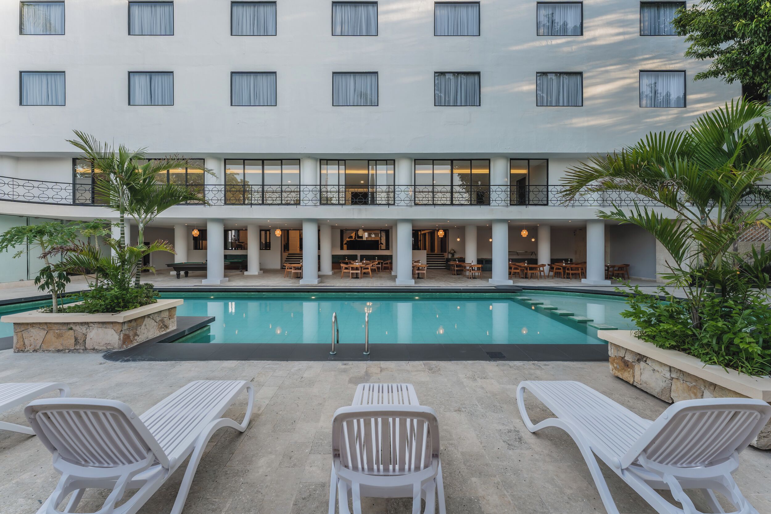 Un patio de hotel con piscina, sillones de descanso y zona de comedor.