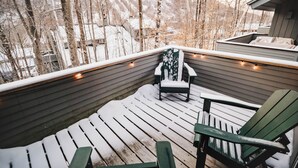 A wooden deck with snow-covered ground and a chair.