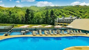 A pool area with lounge chairs and umbrellas, surrounded by lush greenery and mountains.