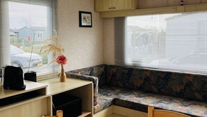 Un intérieur de camping-car compact comprenant une table à manger, des chaises, un petit coin cuisine, un banc rembourré et une fenêtre avec des stores.