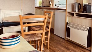 Une cuisine de taille réduite, avec des meubles de rangement en bois, une table à manger avec des chaises, une horloge et un radiateur.
