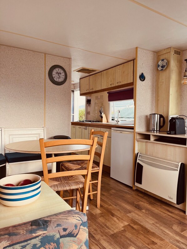 A compact kitchen with wooden cabinets, a dining table with chairs, a clock, and a radiator.