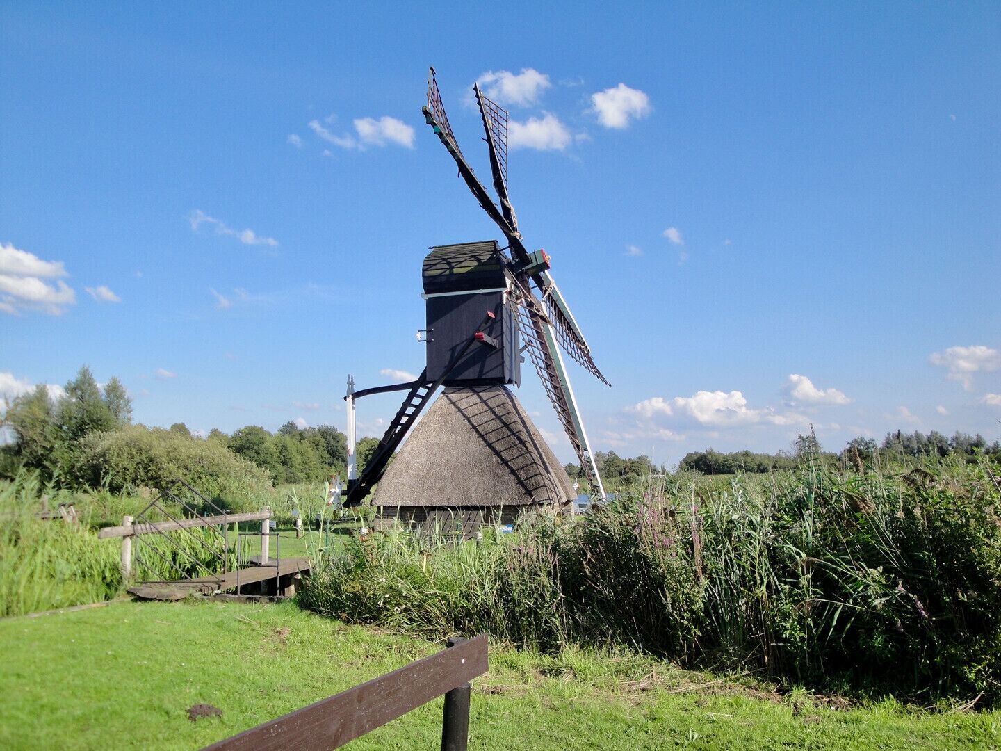 A windmill with a person standing on the platform, surrounded by greenery and a clear sky.