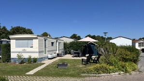 Une maison mobile dotée d’un patio comprenant une table et des chaises, ainsi qu’un petit abri avec un parasol.