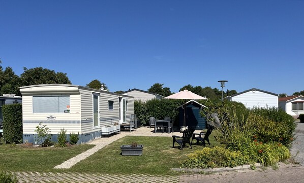 Une maison mobile dotée d’un patio comprenant une table et des chaises, ainsi qu’un petit abri avec un parasol.