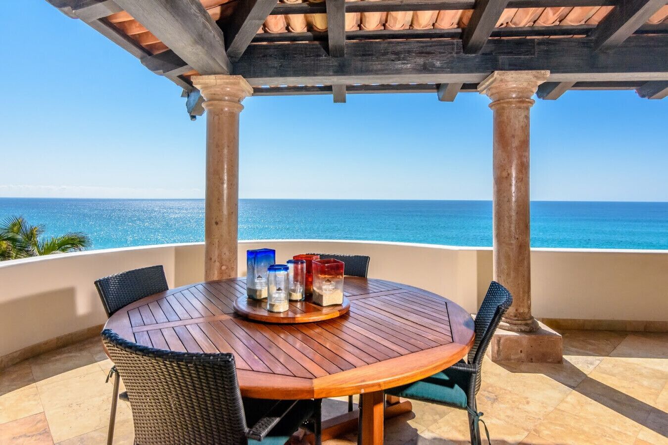 A wooden table with chairs and a tray of salt and pepper shakers, set against a backdrop of the ocean.