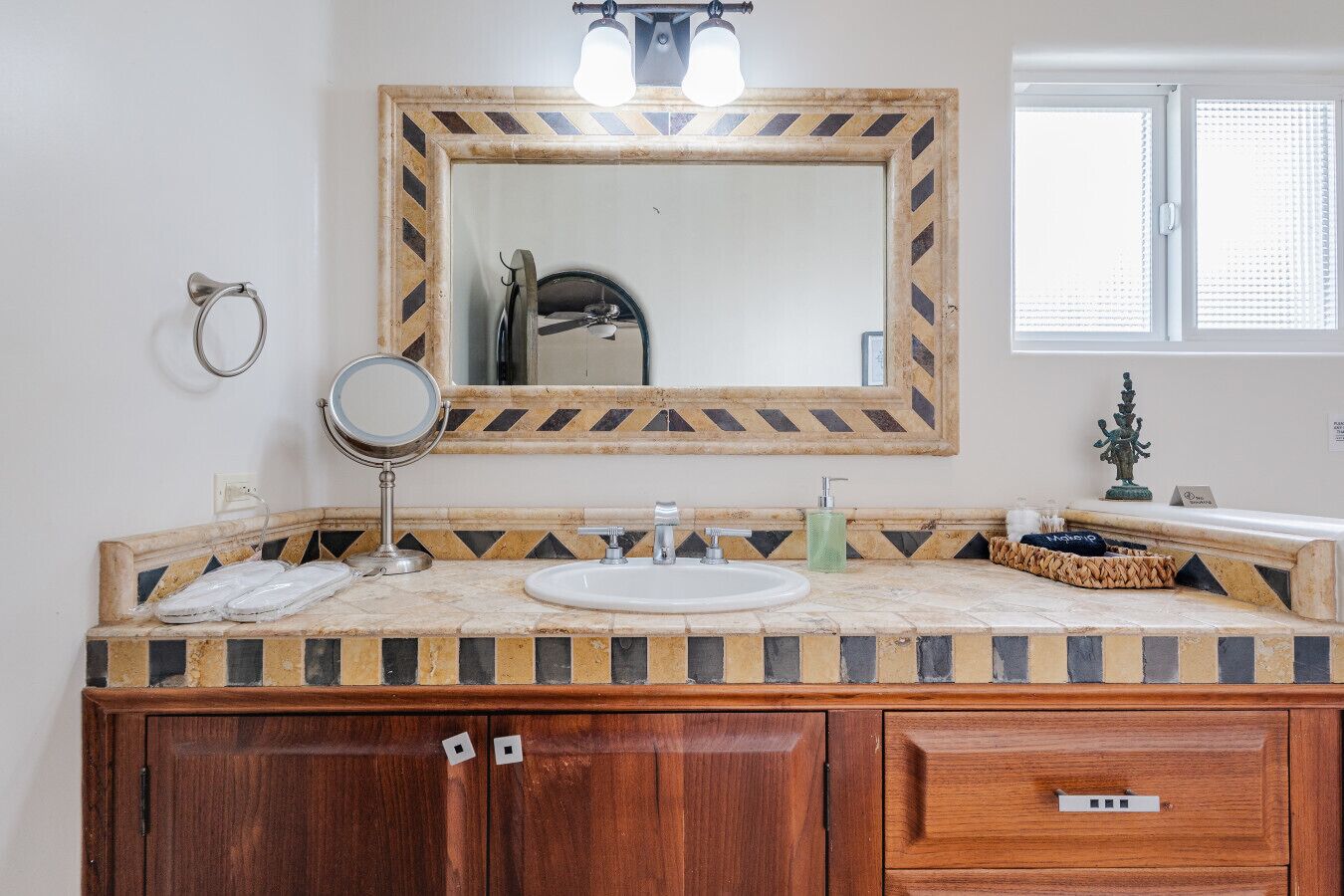 A bathroom with a wooden vanity, a round mirror, a sink, and a decorative mirror frame with a chevron pattern.