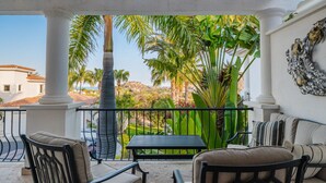 A covered outdoor seating area with a view of a landscaped garden and palm trees.