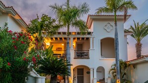 A two-story house with a balcony, palm trees, and a car parked in front.