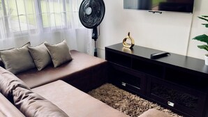 A modern living room with a brown leather sofa, a black entertainment unit, a mounted TV, and a standing fan.
