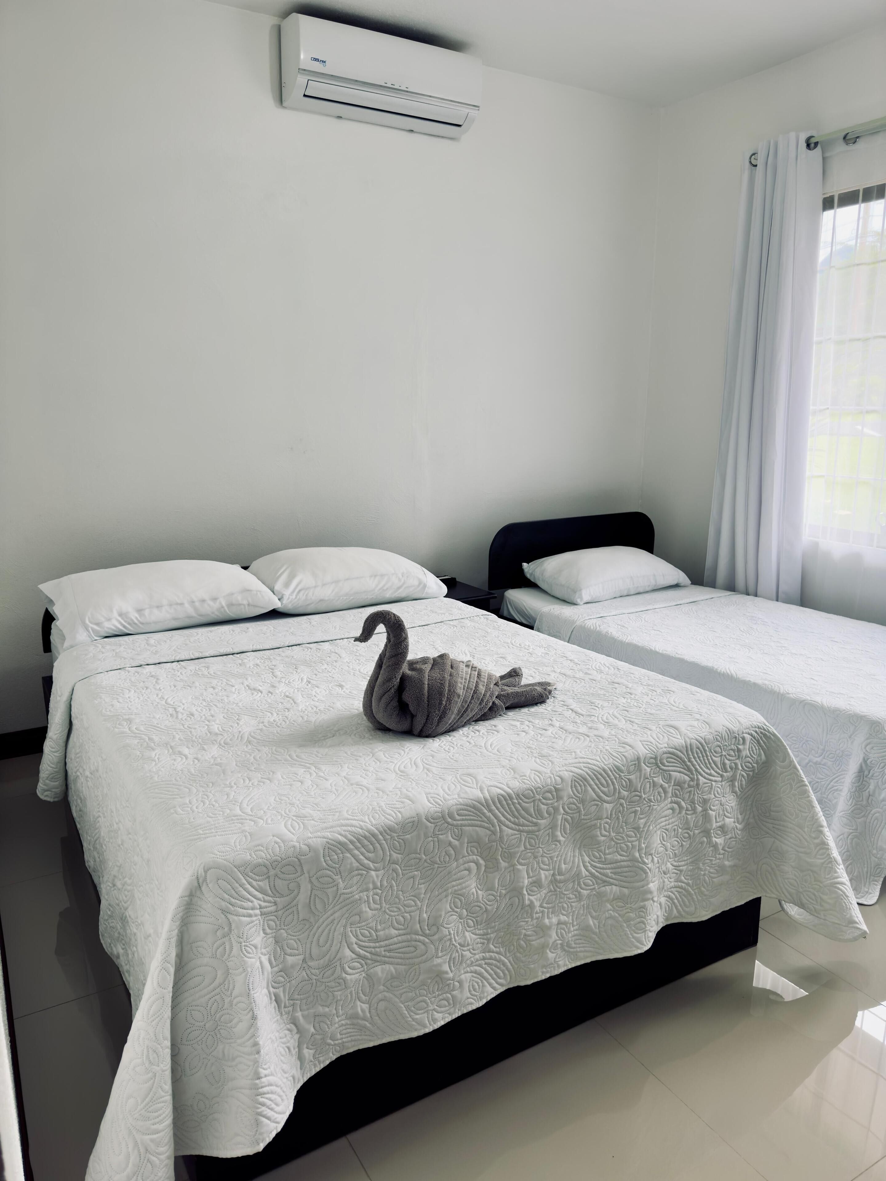 Habitación de hotel con dos camas, aire acondicionado instalado en la pared y una ventana con cortinas.