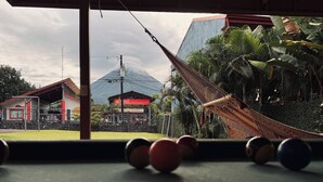 A billiards table with balls in the foreground, a hammock, and a view of a building with a sign reading "Exxon Valdez".