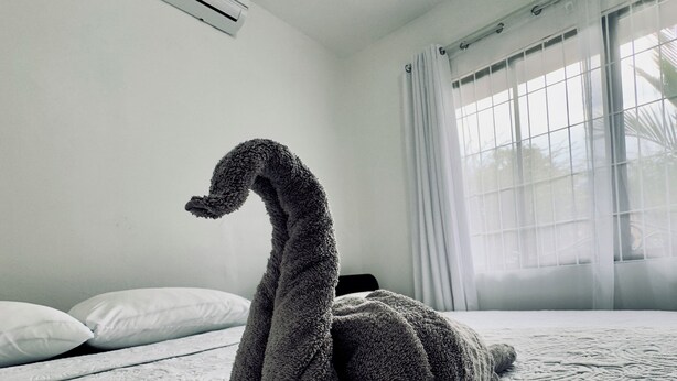 A swan-shaped towel on a bed in a hotel room with a window and an air conditioner on the wall.