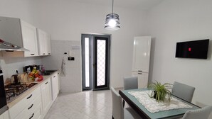 A modern kitchen with white cabinets, a gas stove, and a dining area with a table and chairs. - Vacation Home Southern Geko (Torre del Greco)