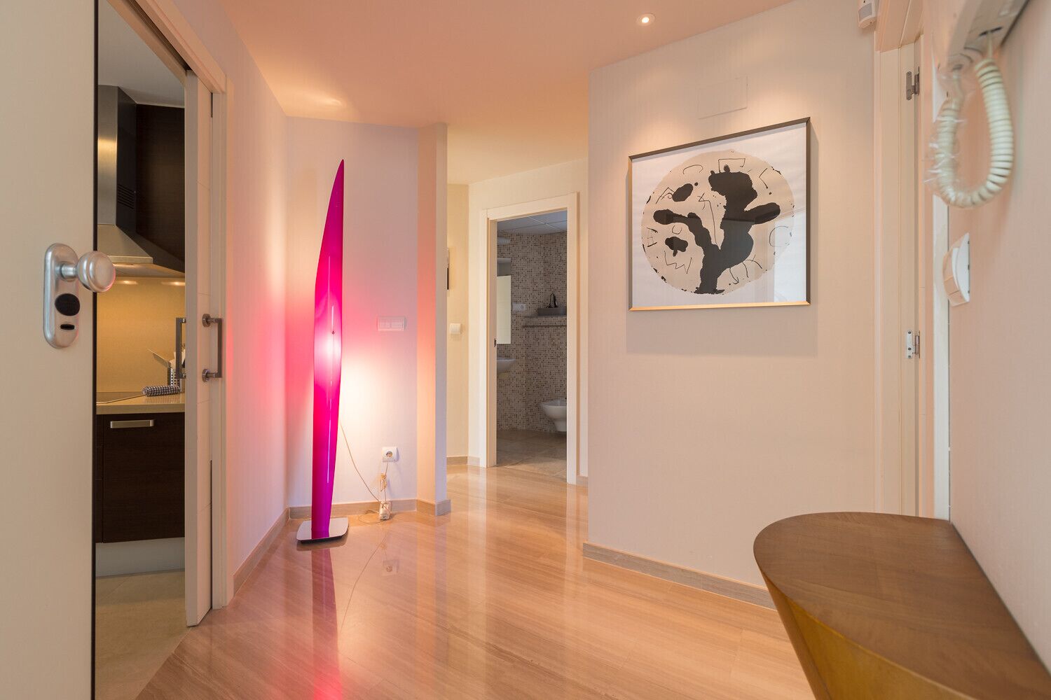 A hallway with a modern kitchen, a pink light sculpture, and a framed artwork on the wall.