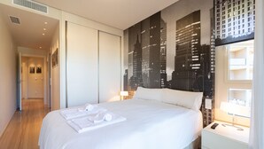 A hotel room with a large bed, a cityscape mural on the wall, a bedside table with a lamp, and a view of the city through a window. - M Rmara in Javea X bia (Javea)