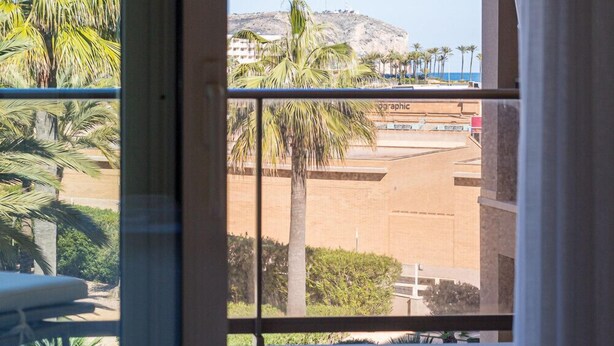 A hotel room with a balcony overlooking palm trees and a distant mountain. - M Rmara in Javea X bia (Javea)