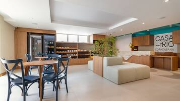A modern hotel lobby with a dining area, a reception desk, and a large plant.