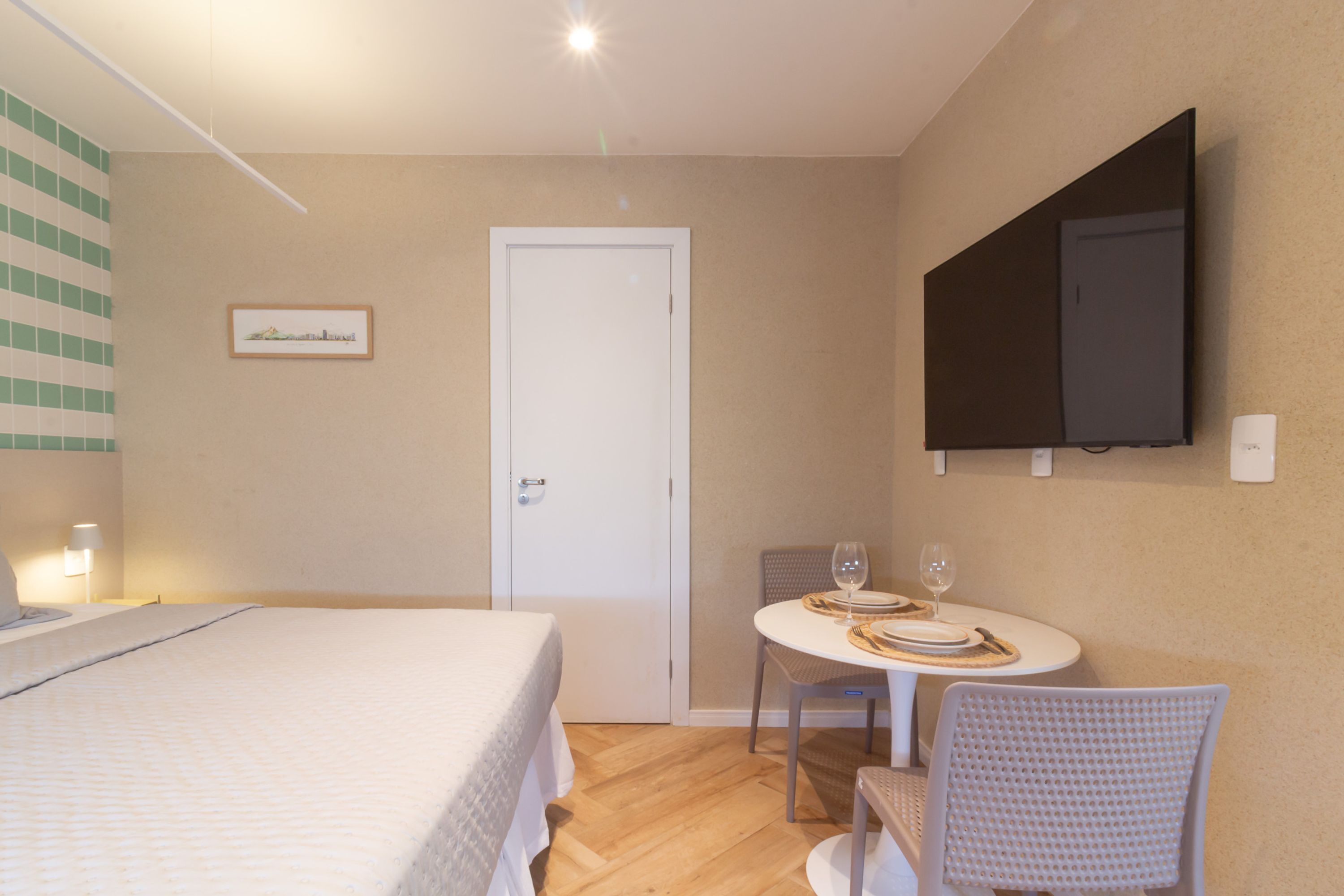 Une chambre d’hôtel comprenant un lit, une table à manger avec des chaises, un téléviseur fixé au mur et une porte.