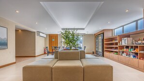 A spacious living area with a large beige sectional sofa, a dining table with chairs, a kitchen area with shelves stocked with food items, and a large window providing natural light. - Cosy a few Steps From Copacabana Beach Q13 e 16 (Rio de Janeiro)