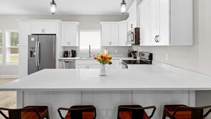 A modern kitchen with white cabinets, a large island, and pendant lighting. - - August Deals - Beach Retreat with private Hot Tub & 5 min. to Navarre Beach (Navarre)