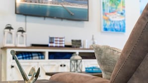 A living room with a television displaying a cityscape, a decorative anchor on a table, and a couch. - - August Deals - Beach Retreat with private Hot Tub & 5 min. to Navarre Beach (Navarre)