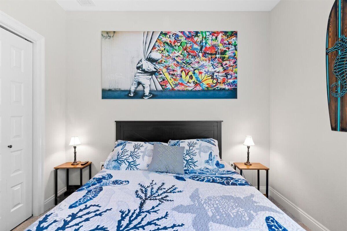A bedroom with a bed, two bedside tables, a wall-mounted artwork, and a wooden seahorse decoration.