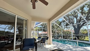 A covered outdoor area with a pool, seating, and a ceiling fan.