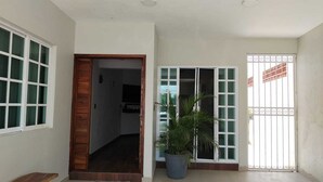 A hallway with a wooden door leading to a room, a potted plant, and a gated window with decorative bars.