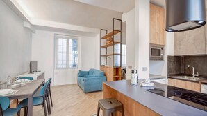 A modern kitchen with a built-in microwave, stove, and sink. There is a dining area with a table and chairs, and a blue sofa in the living area.