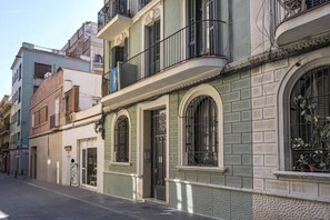 A street view of a building with a green facade, ornate iron gates, and a balcony with a wrought iron railing.