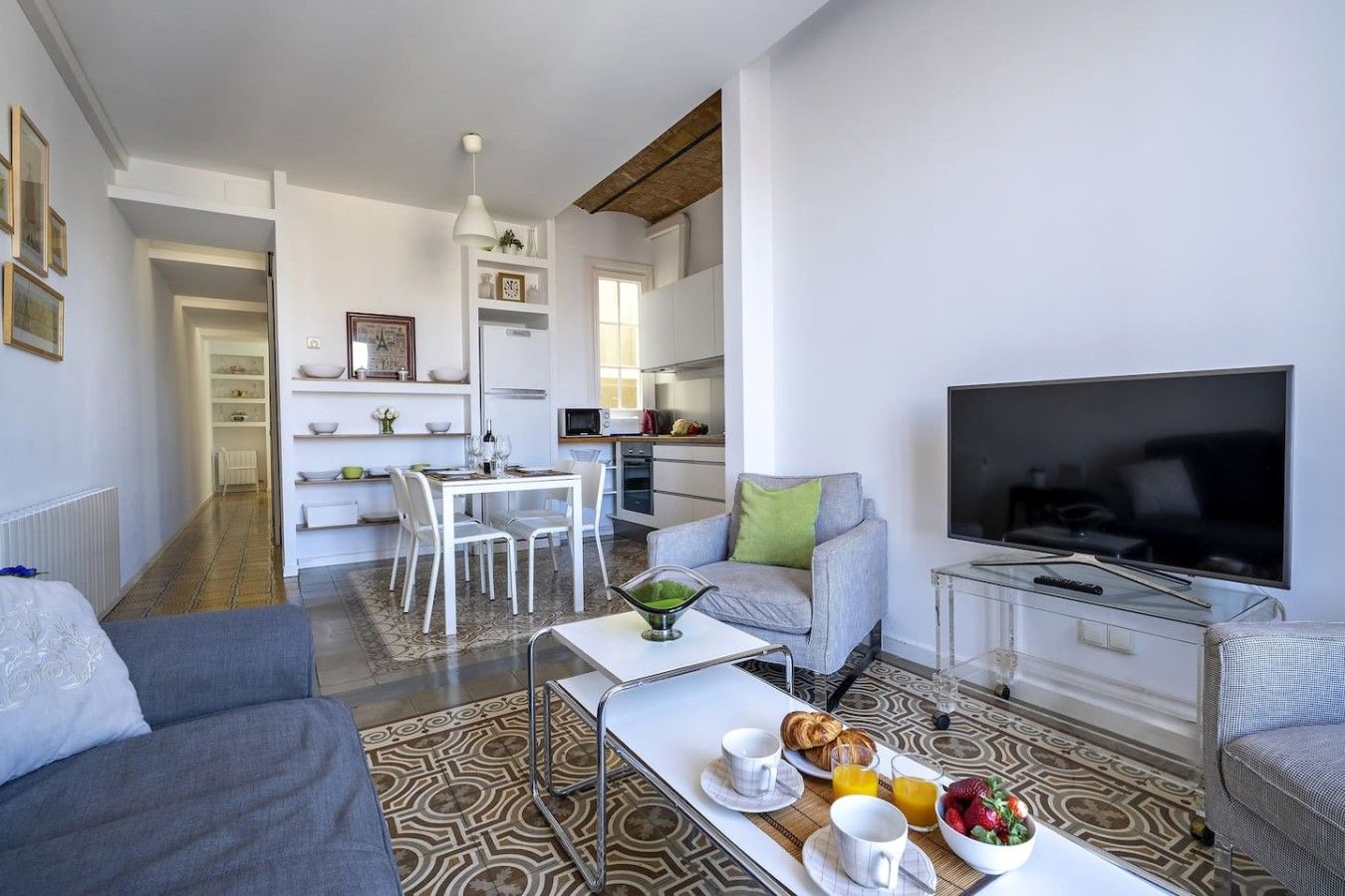 A modern living room with a sofa, a dining area with a table and chairs, a kitchen with a microwave, and a TV.