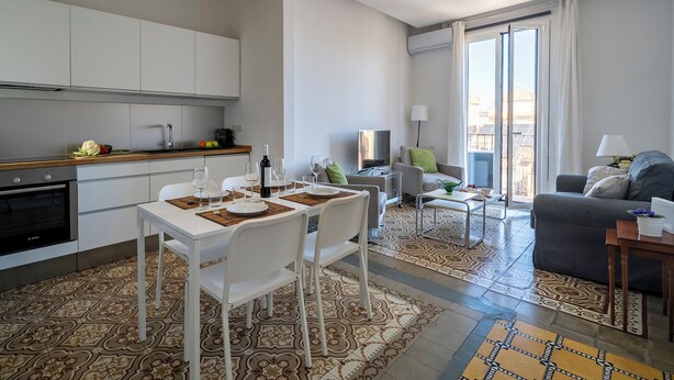 Een modern appartement met een keuken, een eetgedeelte en een woongedeelte. Het heeft een groot raam, een flatscreen televisie en een bank met een salontafel.