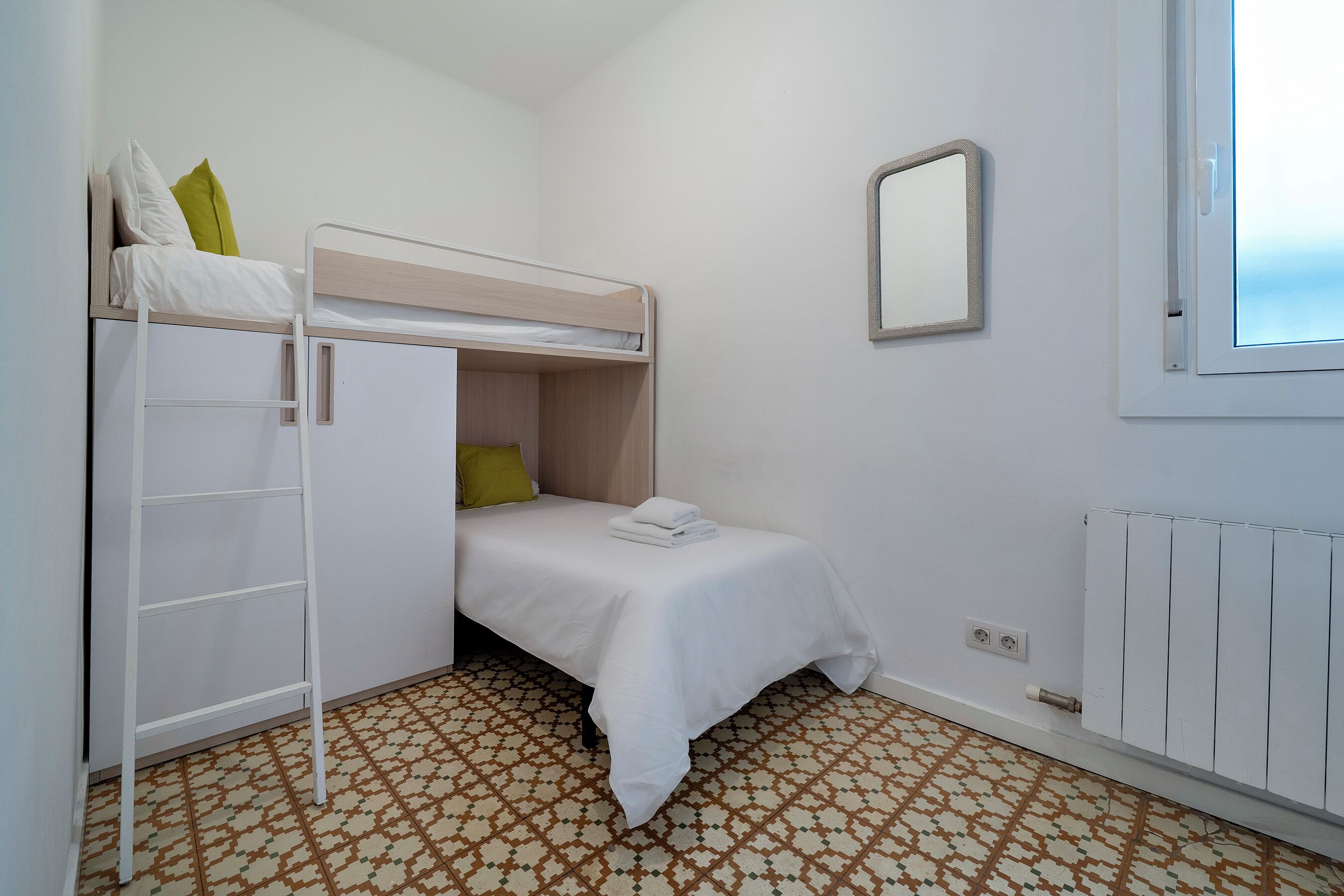 Una habitación pequeña y limpia con literas, un radiador blanco y un suelo estampado.