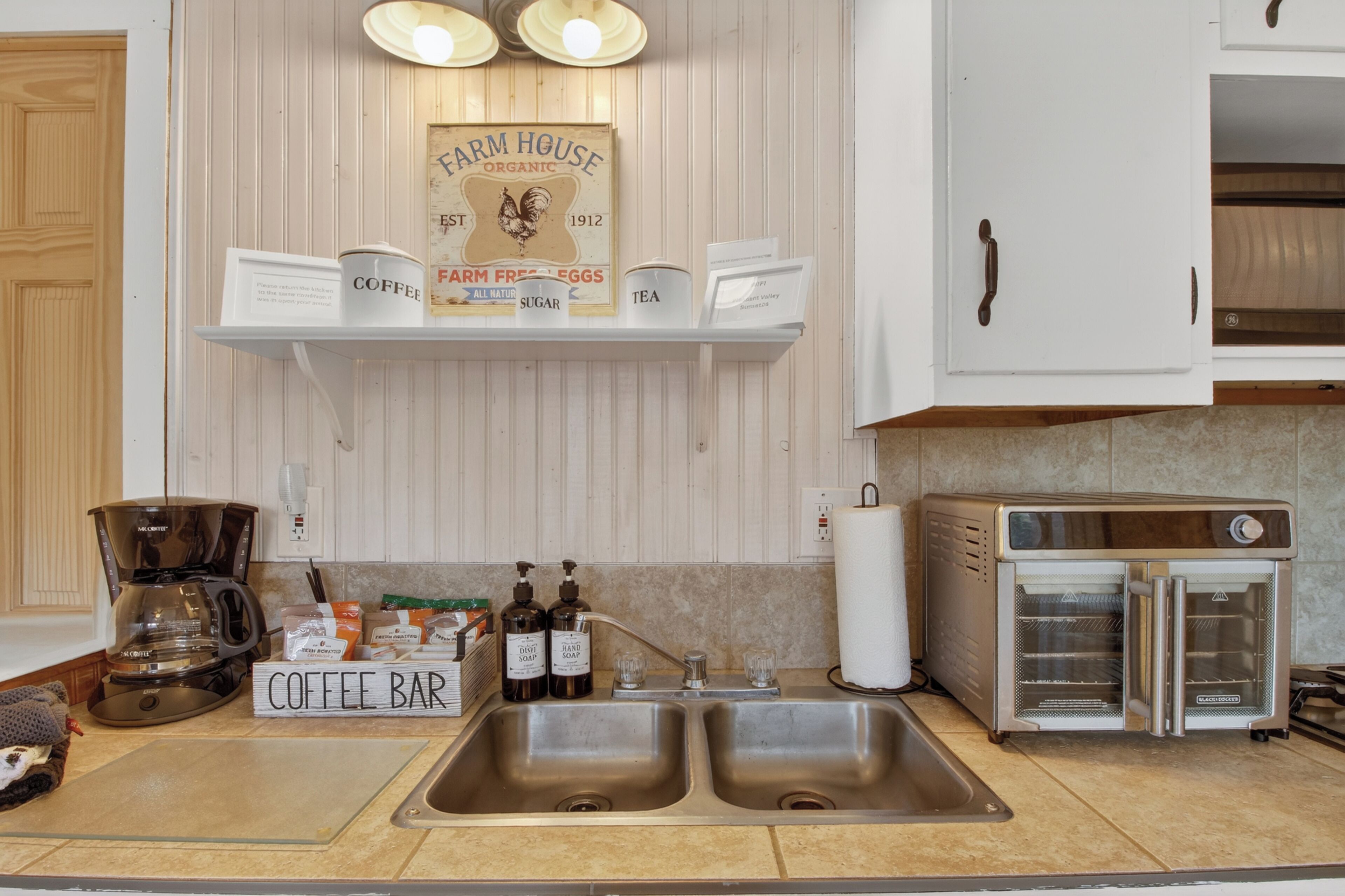 A kitchen with a coffee bar, a Farm House sign, a coffee maker, and a toaster oven.