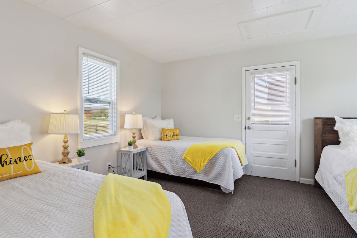 A hotel room with two beds, a door, and a window with blinds.