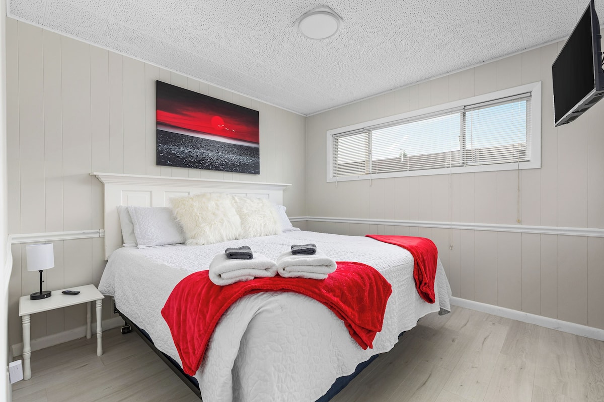 A neatly arranged bedroom with a bed, a nightstand, a TV, and a window with blinds.