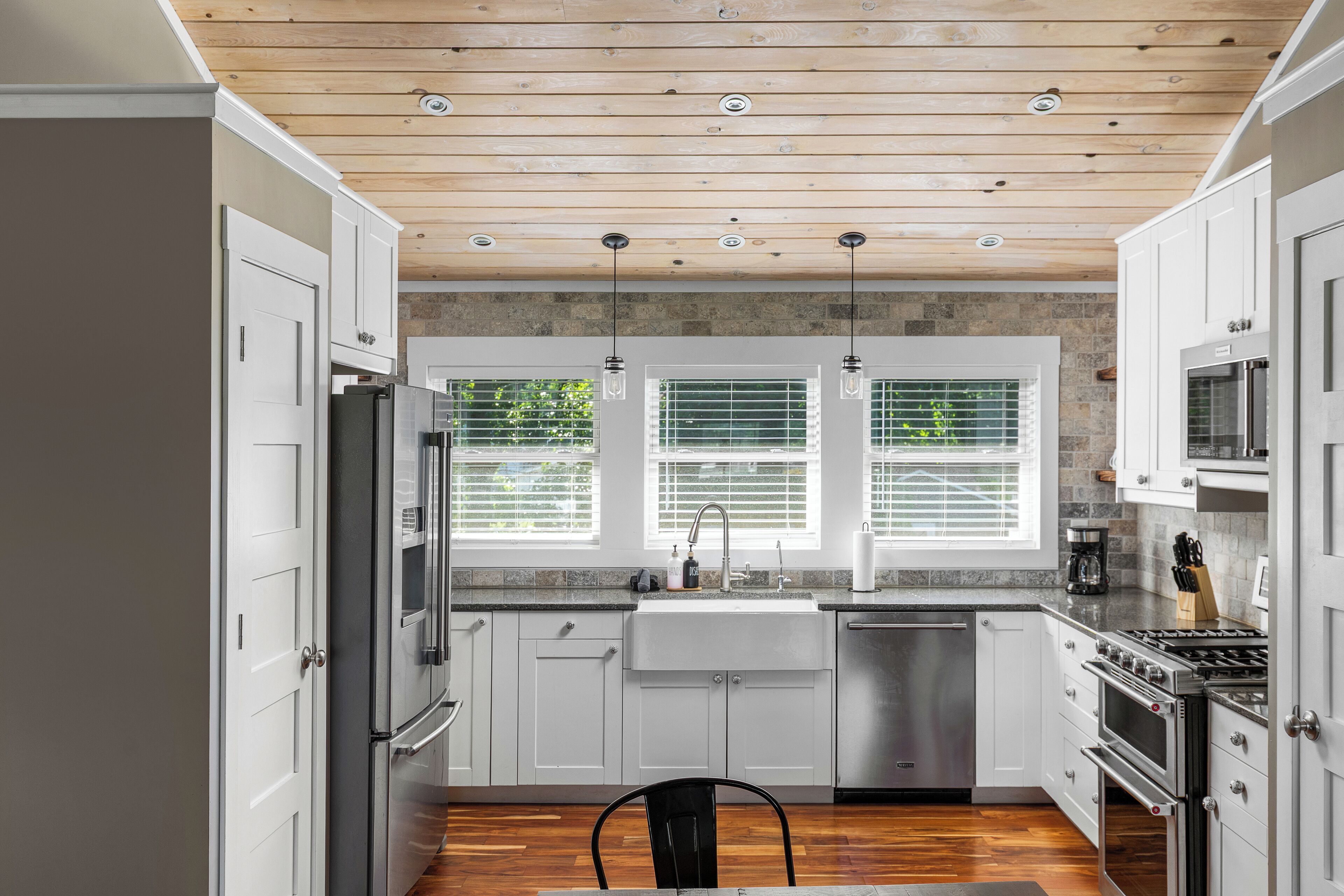 A modern kitchen with white cabinets, stainless steel appliances, and a wooden ceiling.