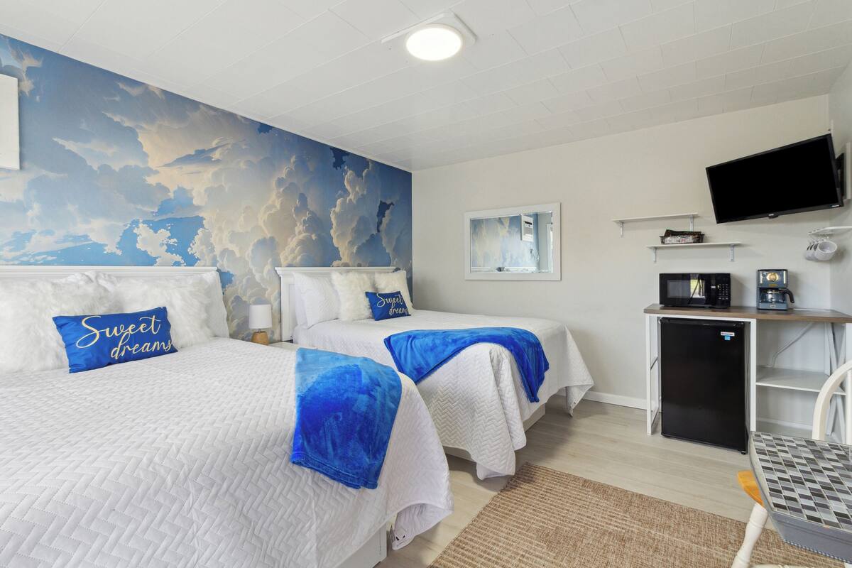 A hotel room with two beds, a TV, a refrigerator, and a microwave.