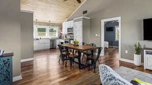 A spacious living area with a wooden ceiling, a dining table with chairs, a grey sofa, and a TV on the wall. - Pleasant Valley Resort (Arcadia)