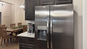 A kitchen with dark wooden cabinets, a stainless steel refrigerator, a granite countertop, and a dining area with wooden chairs and a table.