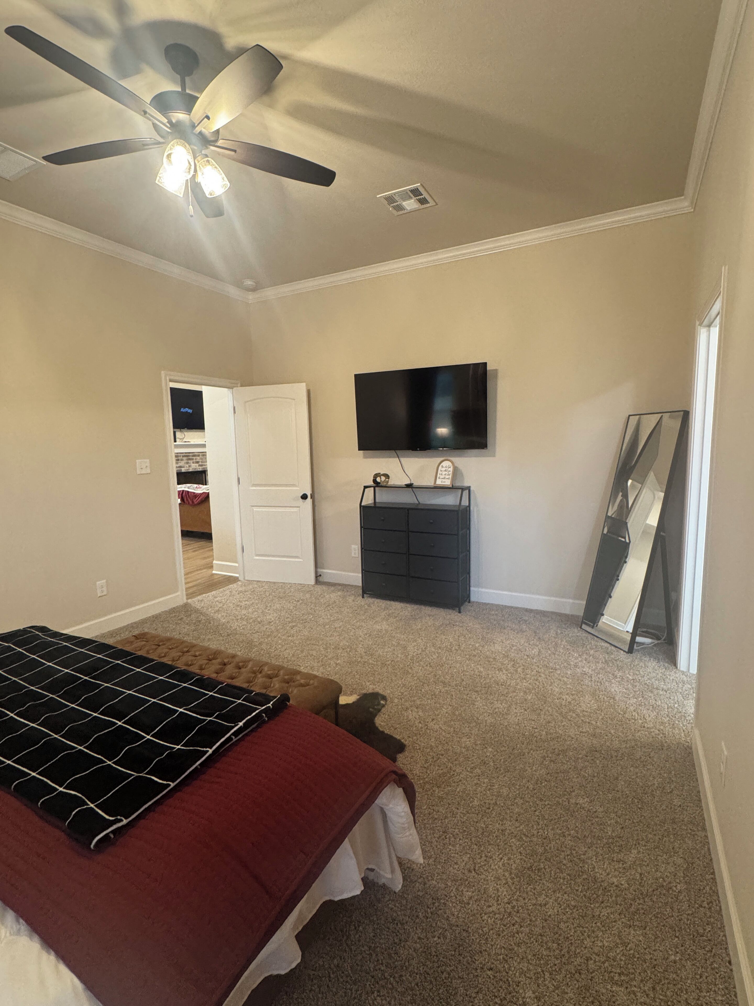 A bedroom with a bed, a ceiling fan, a dresser, a TV, and a door leading to another room.