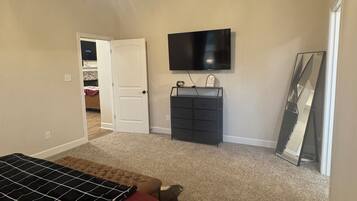 A bedroom with a bed, a ceiling fan, a dresser, a TV, and a door leading to another room.