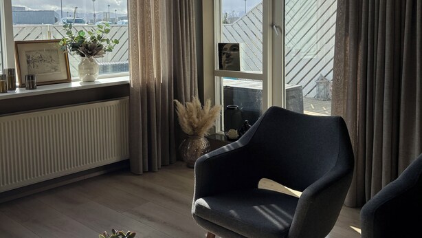Una habitación moderna con un ventanal grande, una silla negra, una mesa con una bandeja de objetos y un radiador.