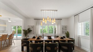 A modern dining area with a wooden table, dark chairs, and pendant lighting. - West Palm Oasis (West Palm Beach)