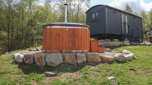 Ein hölzernes Whirlpool mit Schornstein, umgeben von Steinen, und eine kleine Holzhütte im Hintergrund.